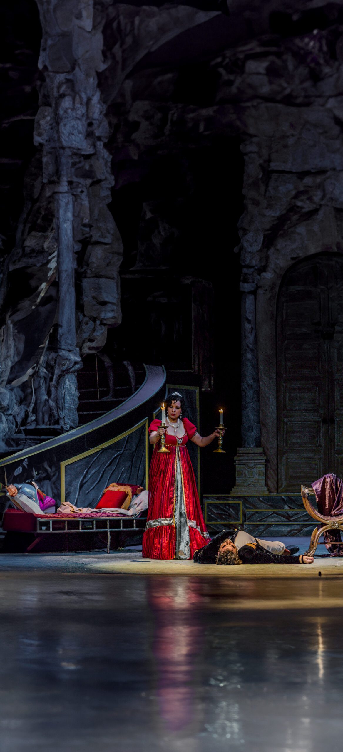 Tosca, from Puccini's opera, holds a pair of burning candles over the dead body of Scarpia in a stage production.